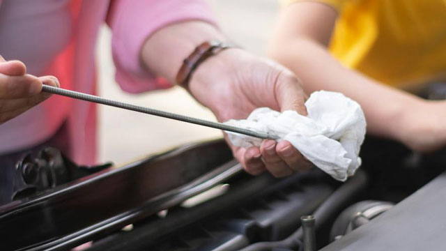 A hand of a father in a pink sleeve can be seen wiping the oil checker of a car next to a child in yellow shirt
