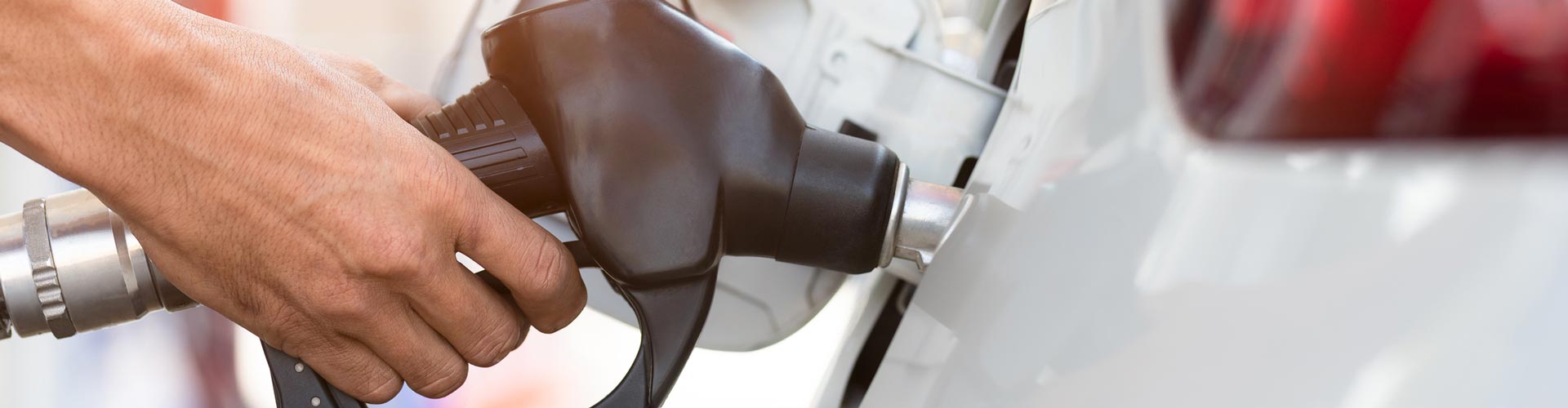 A hand on a fuel bowser putting fuel in a white car