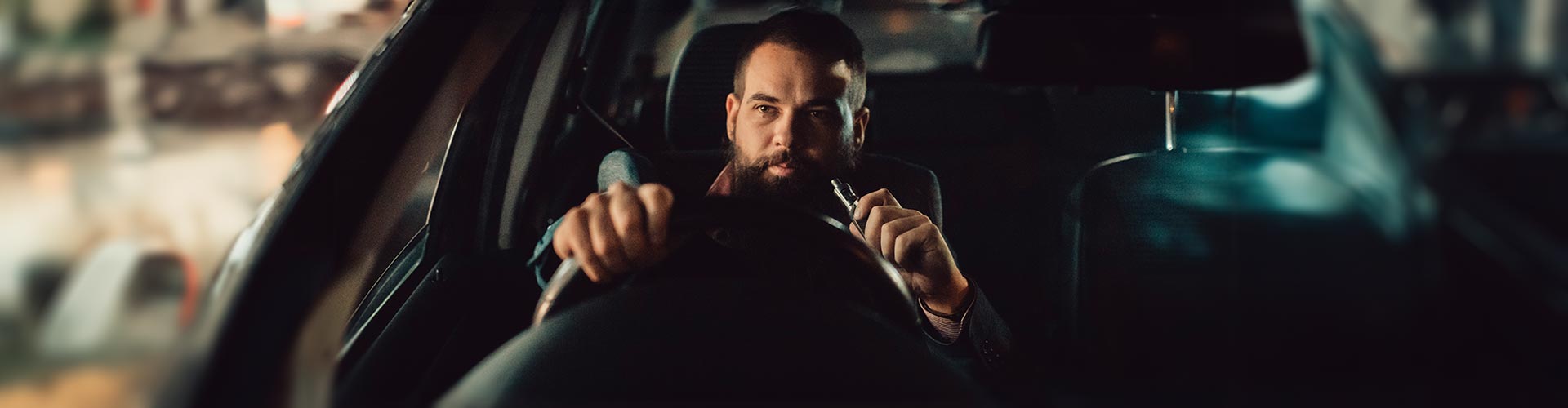 A man sits in a car with a vape in his hand