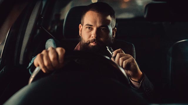 A man sits in a car with a vape in his hand