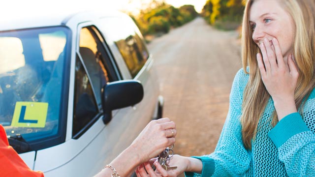 A mother gives her nervous daughter car keys. On the car is an L plate