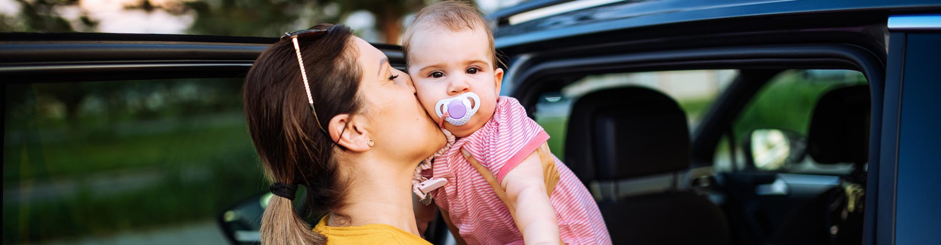 A mother kisses her baby before putting her in her baby seat