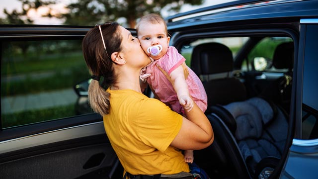 A mother kisses her baby before putting her in her baby seat