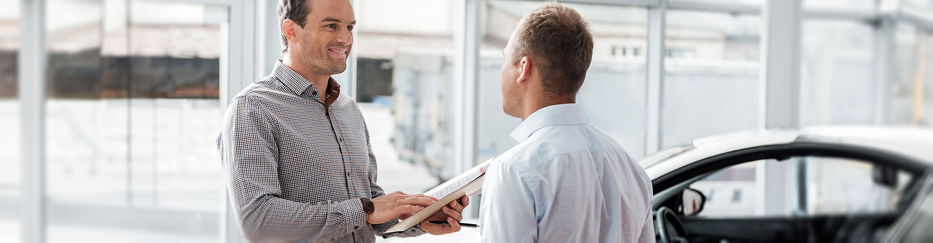 Two men wearing collared shirts discussing the price of a car in a dealership
