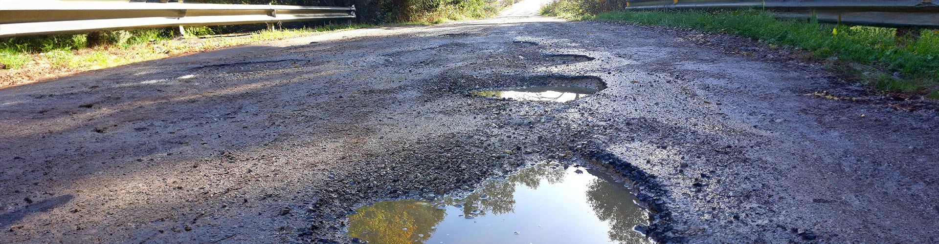 Low angle photo of potholes filled with water on a country road