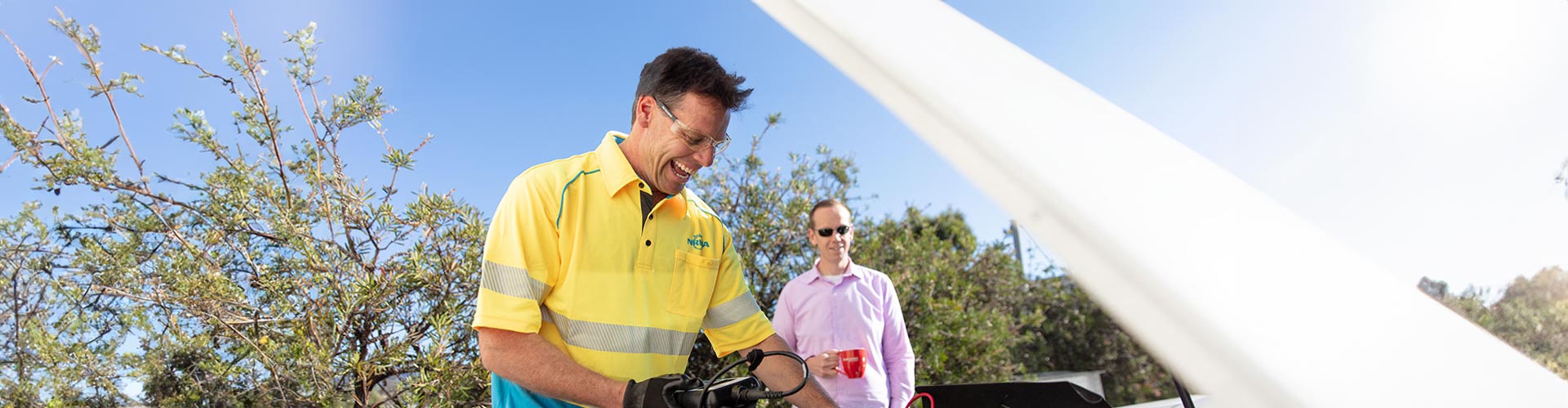 A roadside assistance technician check a car battery while the owner stand behind