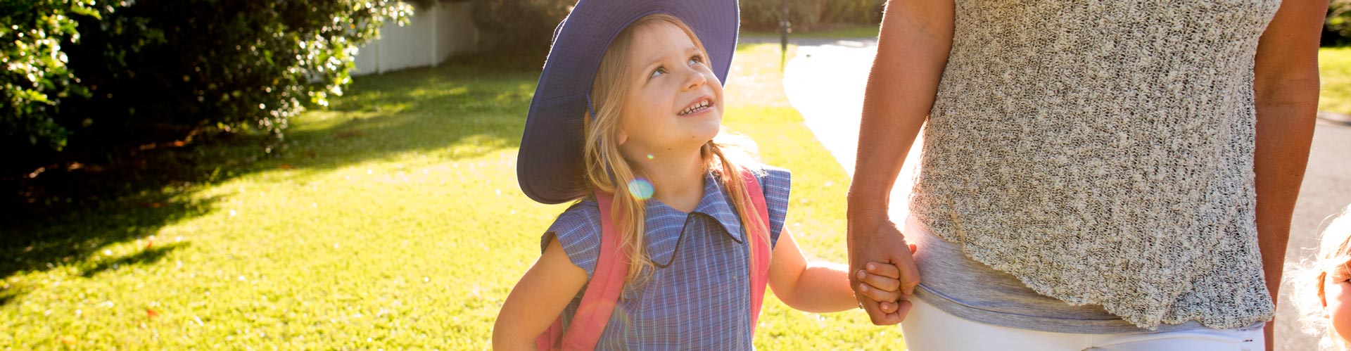 Young girl in school uniform holds her mum's hand and looks up at her