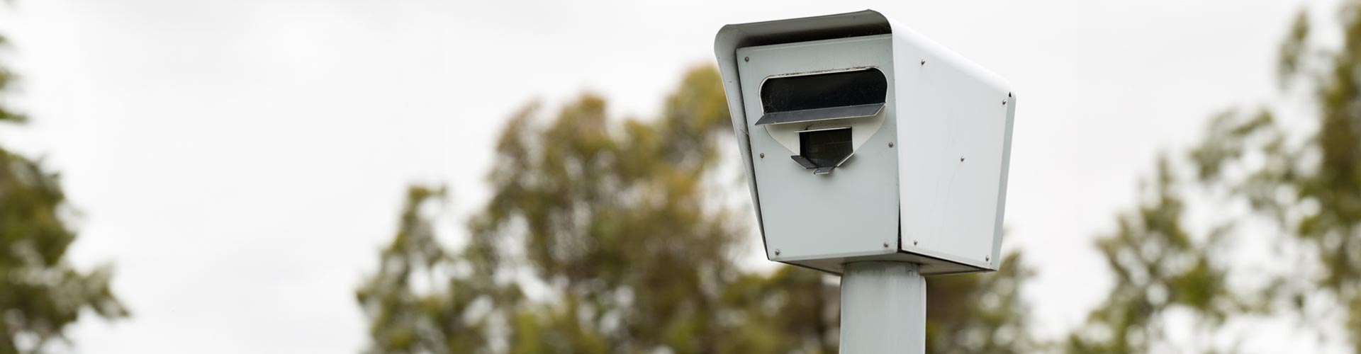 A red light camera against blurry trees