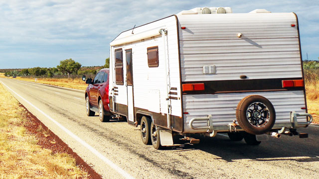 An SUV and caravan are parked on an outback road stretching into the distance