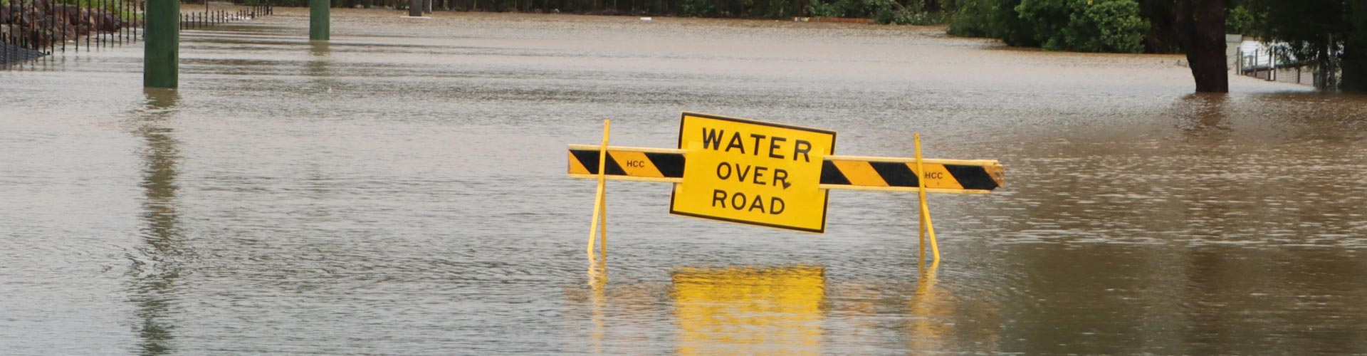 A sign that says "Water over road" sits in middle of flooded road