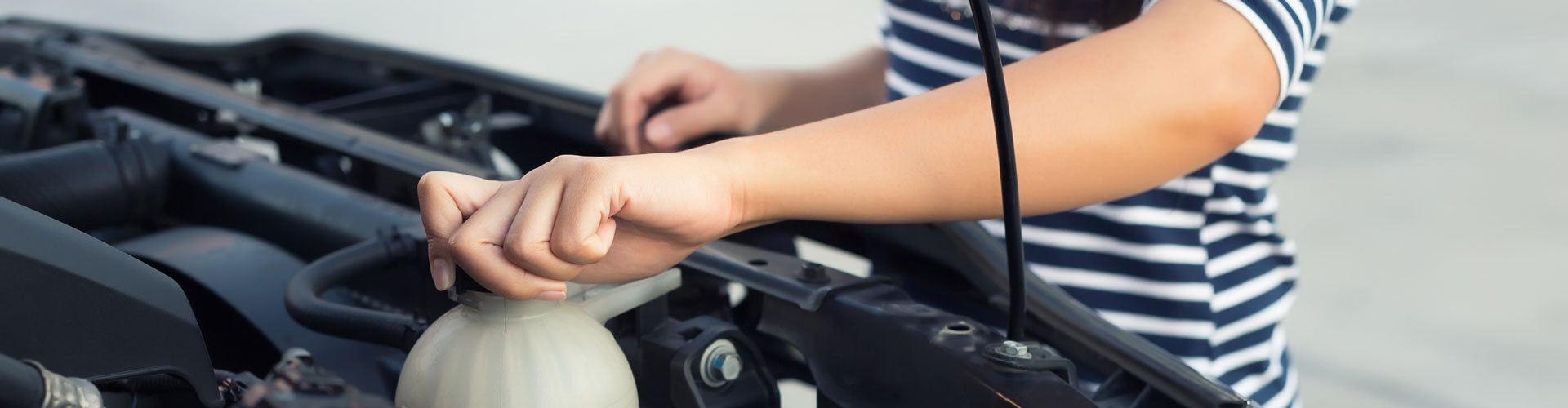 Woman in striped top checking the coolant level on her vehicle