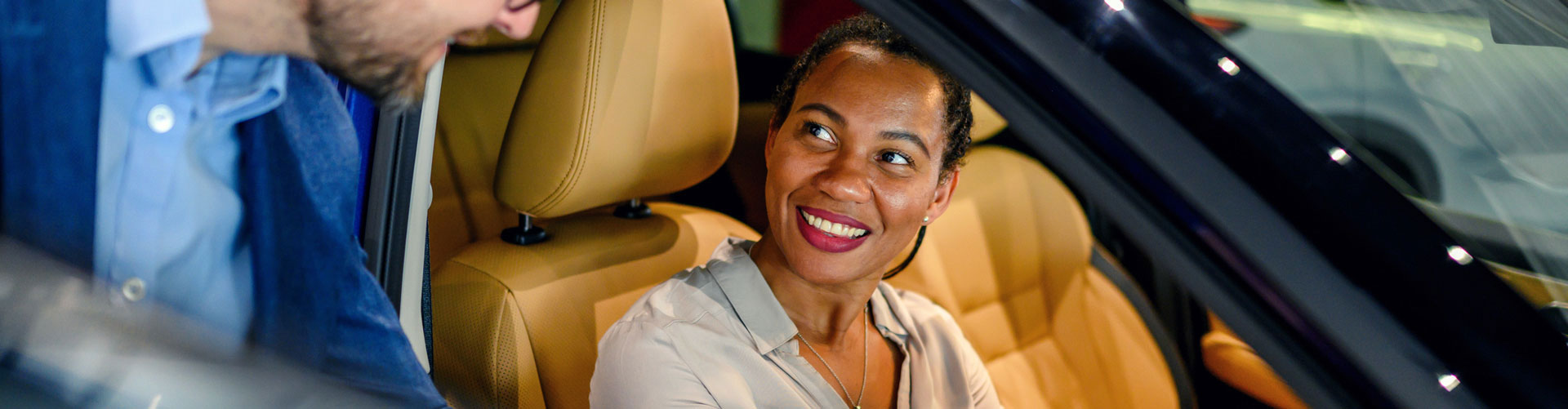 Woman sitting in car while dealer stands outside it pointing at something