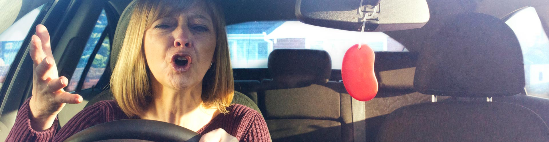 A woman sits in the driver's seat of a car and is mouthing off at someone else