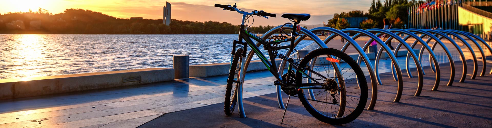 Sun bursting out above the horizon and Lake Burley Griffin with a bicycle parked near the lake water.