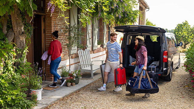 A man and woman carrying travel bags out of an open car
