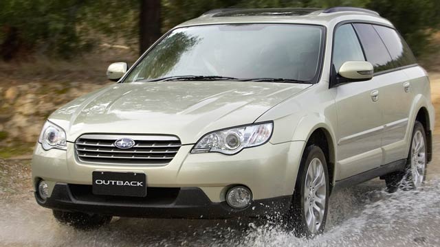 Gold 2004 Subaru Outback driving through a puddle on a dirt road