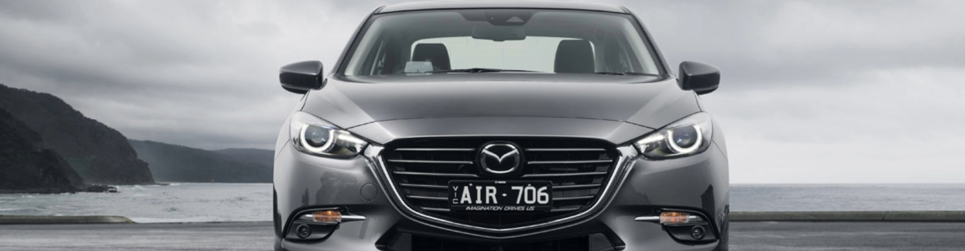 2016 Mazda3 Astina sedan grey Close up of a grey, metallic 2016 Mazda3 Astina parked on the beach with the sea and grey sky behind