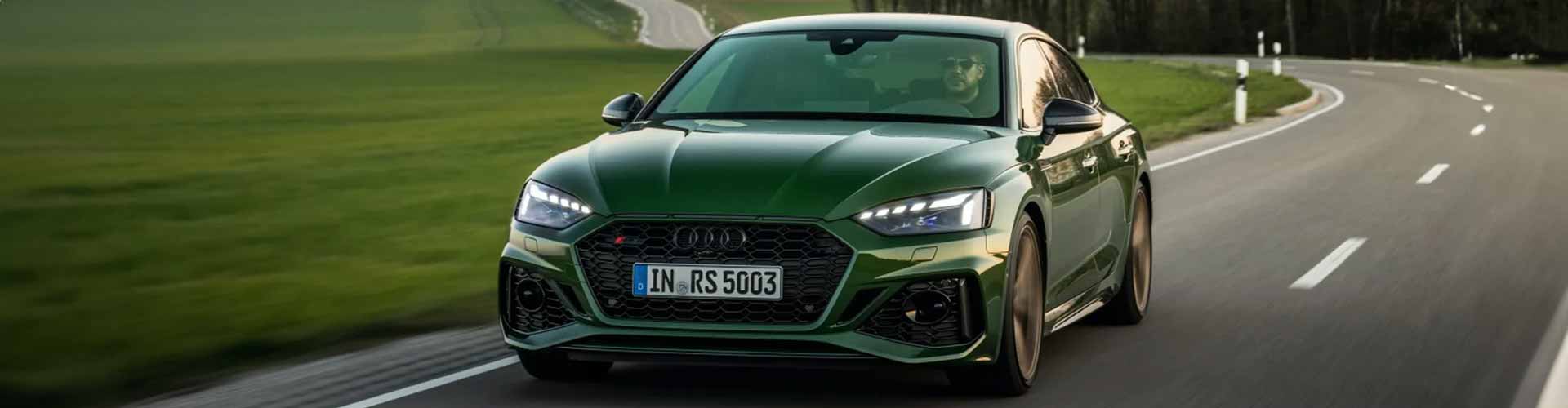 Front view of a sporty green Audi sedan travelling along a road in the countryside.