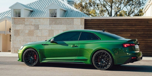 Side view of a sporty green Audi sedan parked beside a stone and wood home exterior wall.