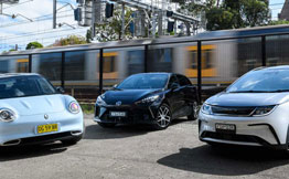 Three small EVs parked in front of fast moving train