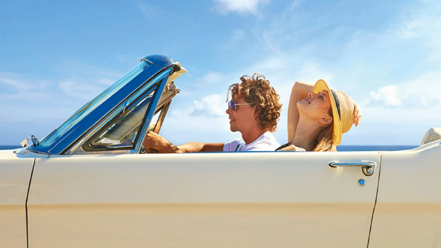 Man and woman enjoying a seaside drive in a white vintage convertible