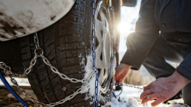 Close-up of a man's hands installing chains on a tyre in the snow