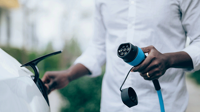 A person wearing a white shirt, holding an electric vehicle charger.