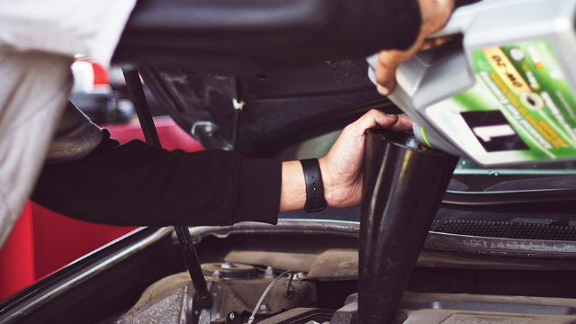 Side view of a driver topping up a car engine with motor oil