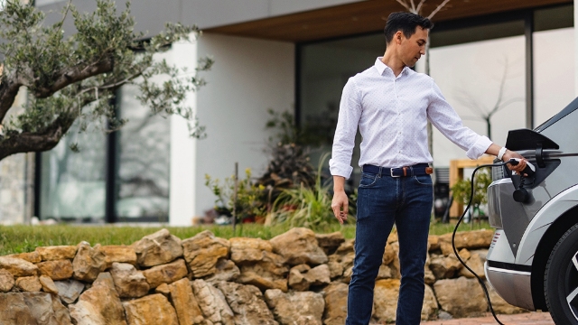 A person plugs their EV in to charge in their driveway