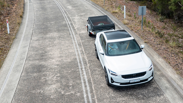 A white Polestar EV tows a trailer on a country road