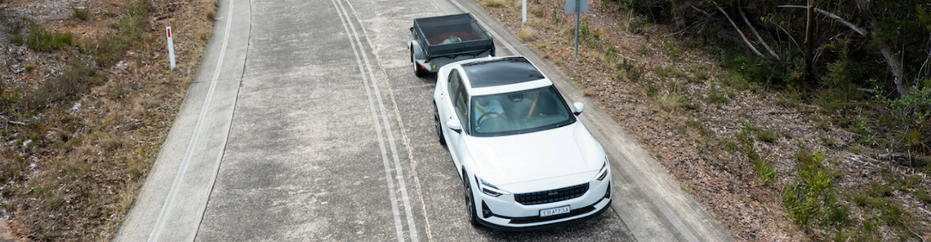 ev-towing-trailer-1920x500 A white electric vehicle towing a small trailer along a road in the country.
