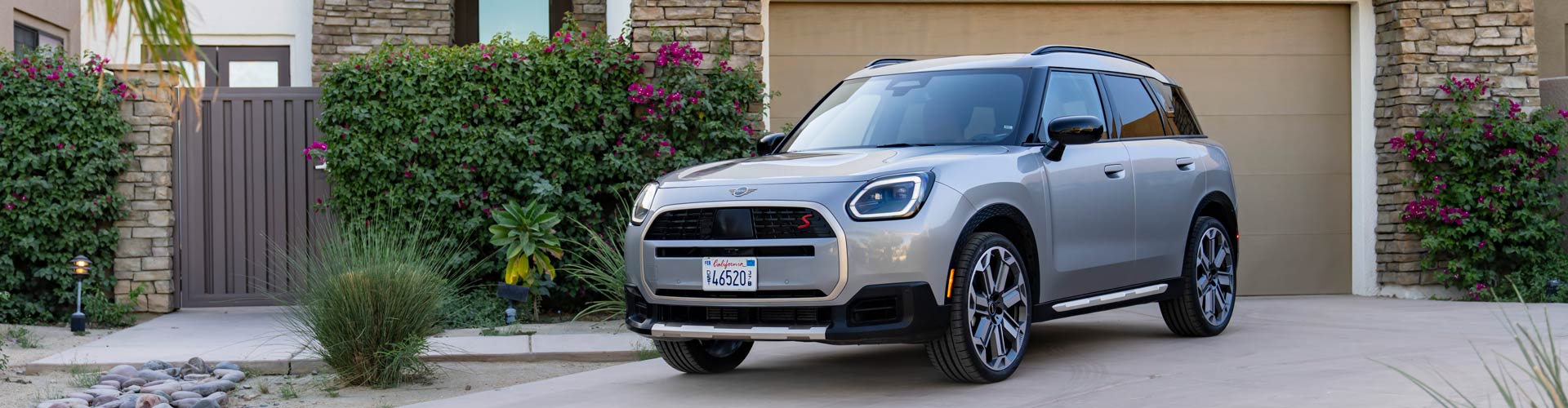 The electric 2024 Mini Countryman S parked outside a house on a driveway next to a flowering bush