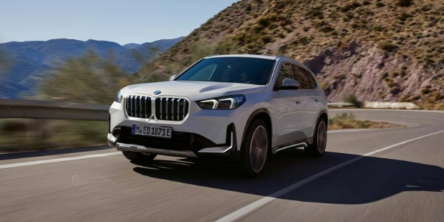 Front-angle view of a BMW iX1 e-Drive driving up a steep and windy road.