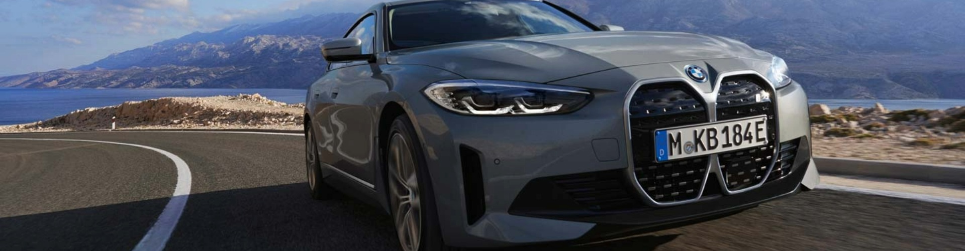 Front-angle view of a grey BMW driving up a steep road with a picturesque view in the background.