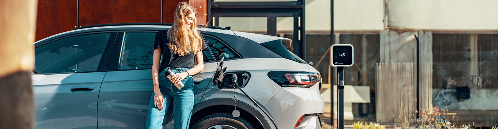 A woman leaning up against her car as it charges electrically A woman leaning up against her car as it charges electrically