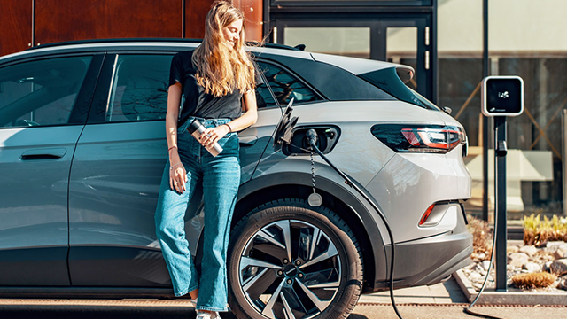 A woman leaning up against her car as it charges electrically 