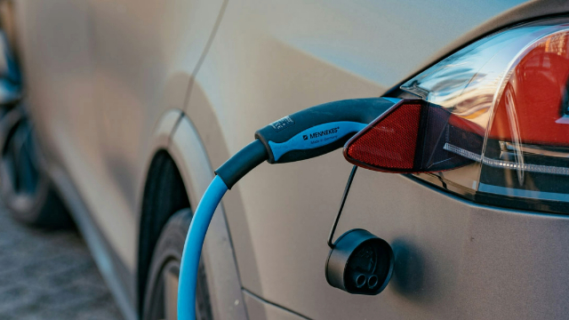 A blue charging cable attached to the side of a gold colour car near the rear light.