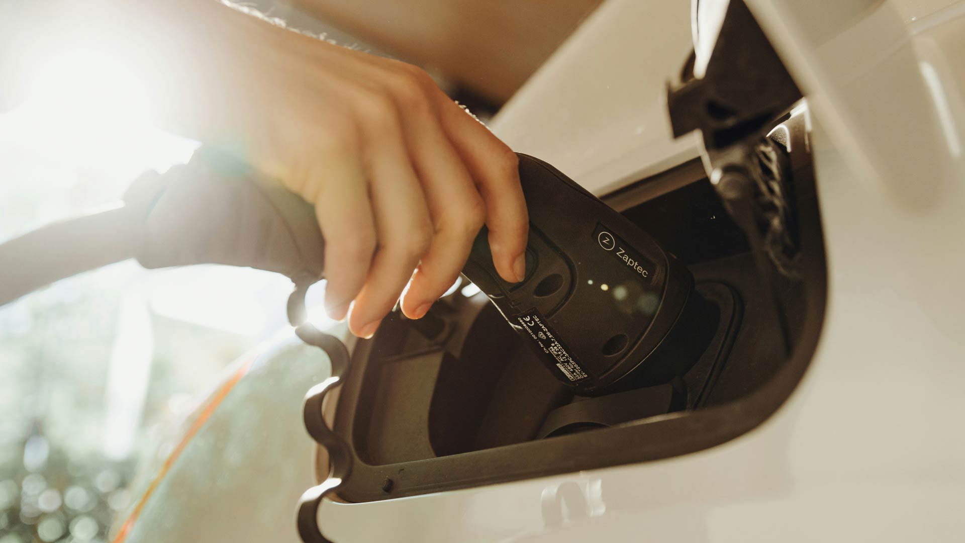A hand plugs in a white EV with a curly cable