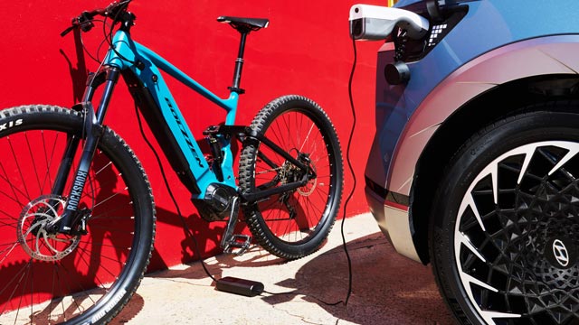 A Hyundai Ioniq 5 charges an e-bike against a red wall