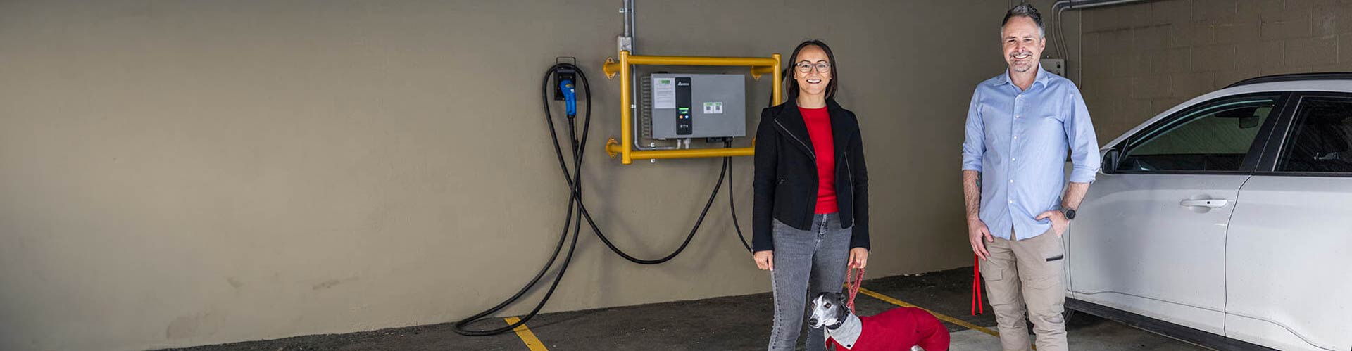 Two people and a dog standing near an EV charging in an apartment carpark