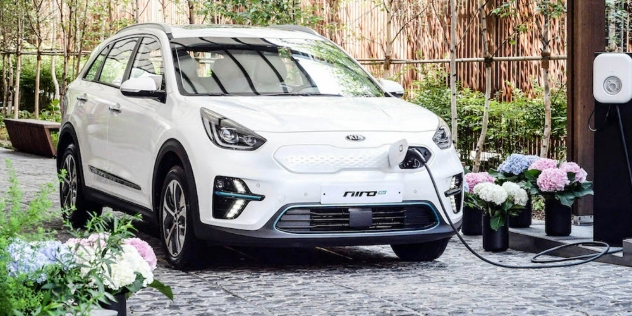 A white Kia e-Niro with a charging cable plugged into the front.