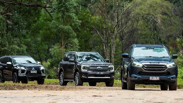 Three utes driving on a road with trees in background