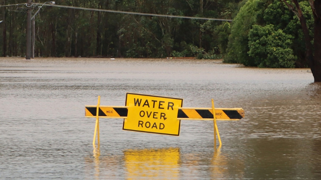 water over road written on a yellow caution sign on a flooded road