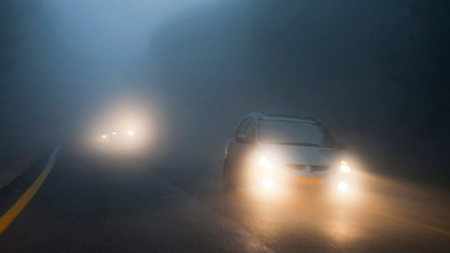 Cars with fog lights switched on driving on a foggy country road