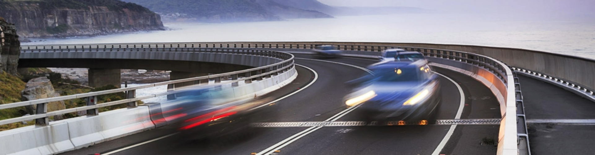 Cars driving along a coastal road at dusk Cars driving along a coastal road at dusk