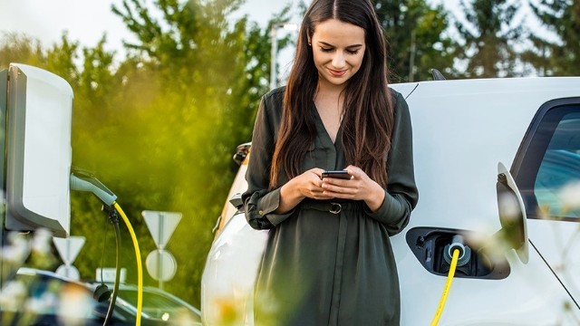 A person smiles using their phone as their EV charges in the background