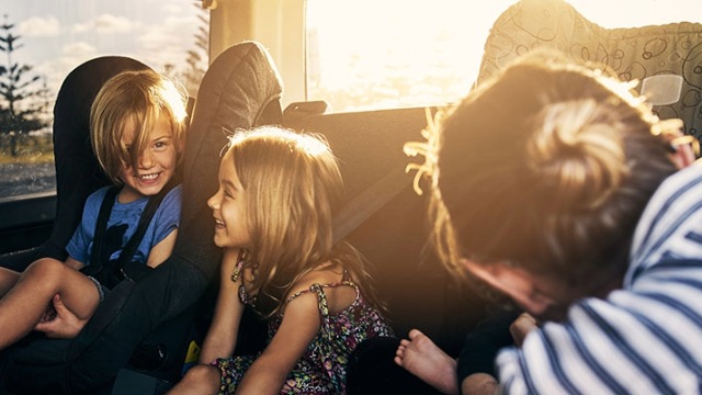 A parent reaches in to back of car to secure children in their seats