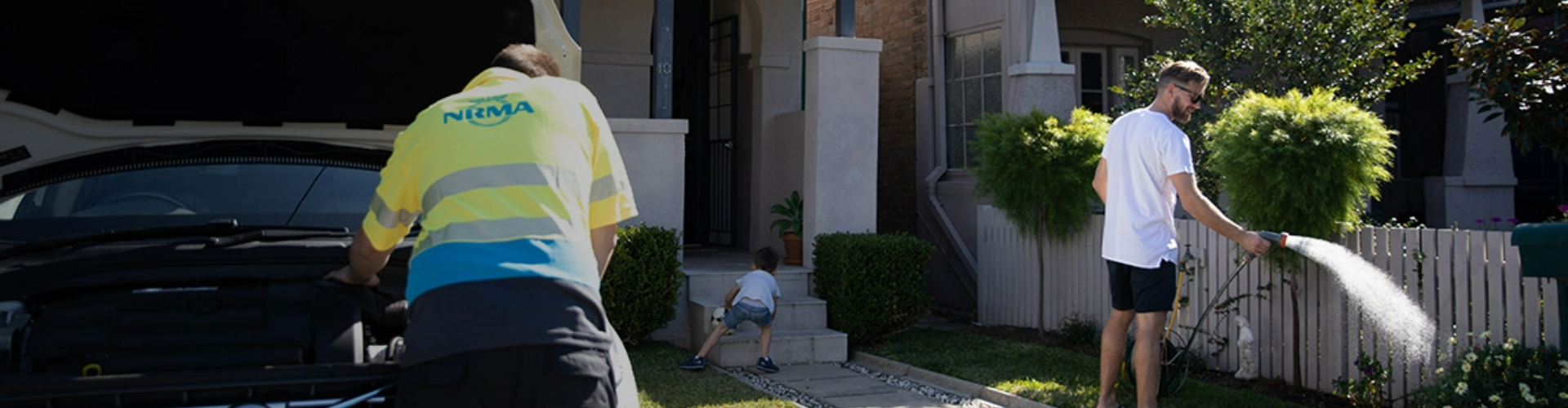 NRMA technician working under a car bonnet in the driveway of a family home NRMA technician working under a car bonnet in the driveway of a family home