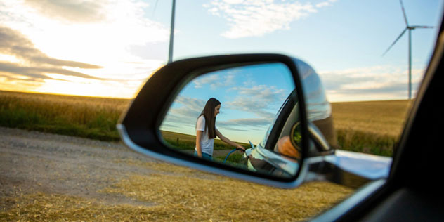 Reflection of a woman charging an EV in the car mirror