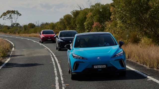 A blue MG EV drives along a country road followed by other vehicles